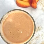 photo of a peach smoothie on a white background pictured with a small pile of sliced peaches